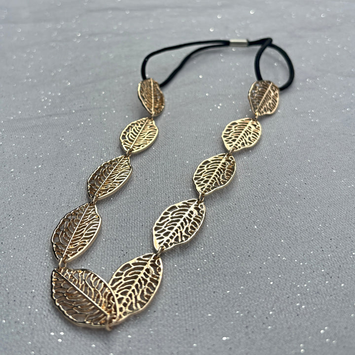 Leaf headband, gold tone metal leaves with intricate cutout detailing, linked design, black elastic fastening for secure fit, nature inspired accessory, elegant vintage style headpiece, chic statement hairband, stylish gift for her