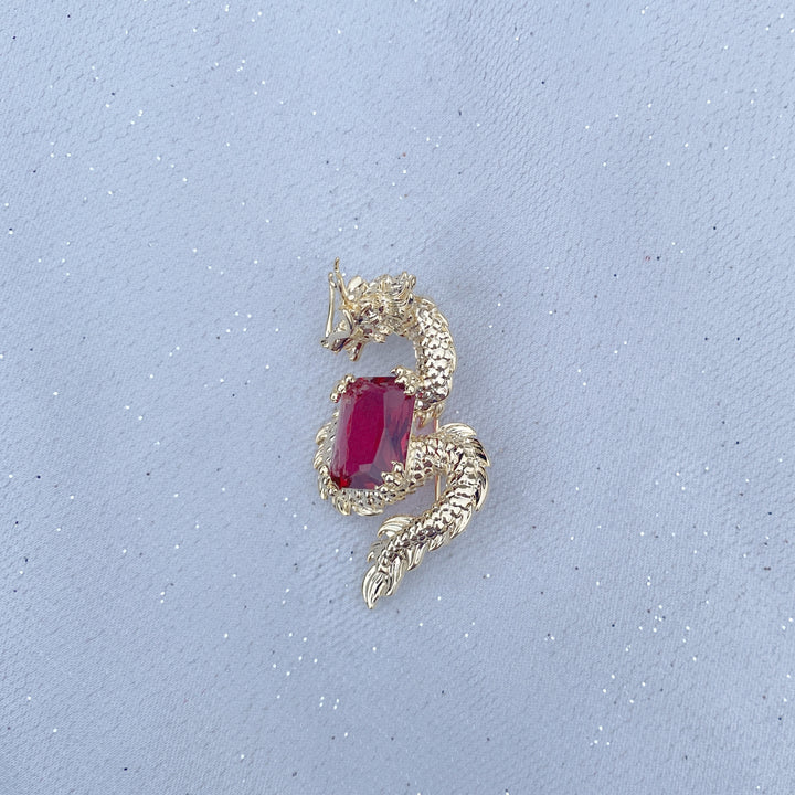 Gold dragon brooch wrapped around a large red gemstone.