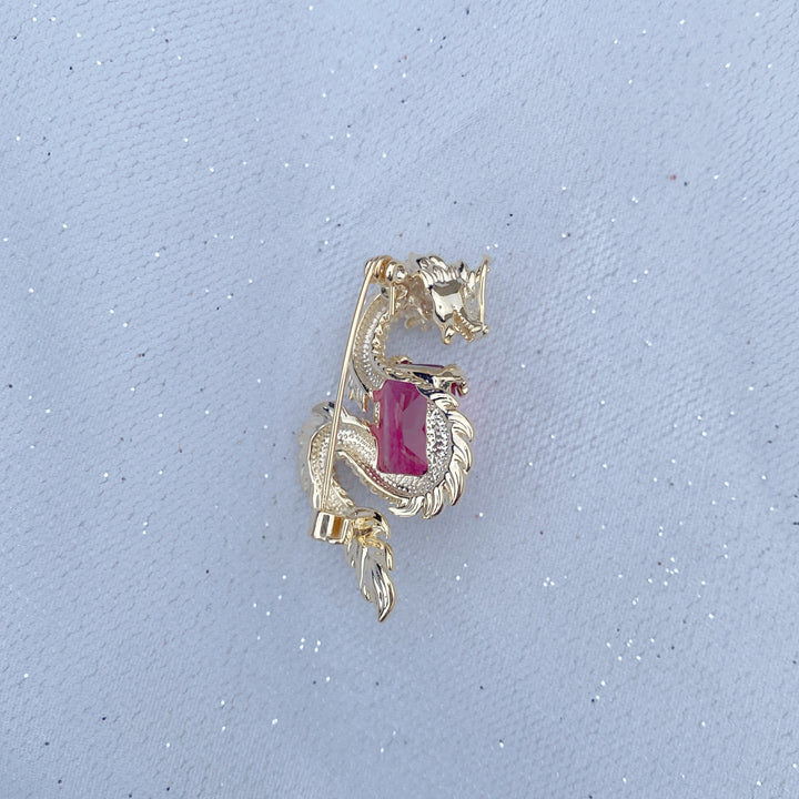 Gold dragon brooch wrapped around a large red gemstone.