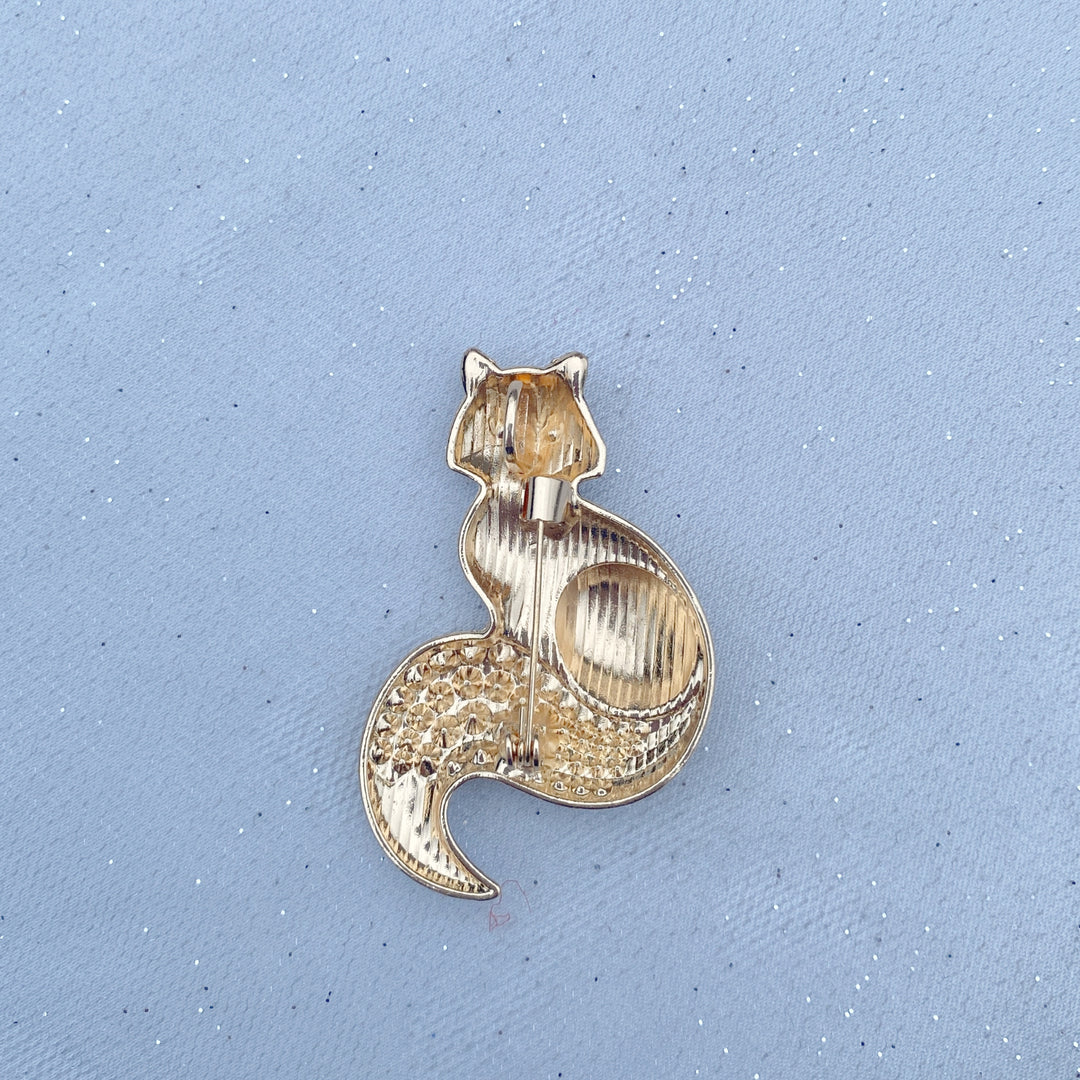 Brown and white fox brooch with blue eyes and an orange crystal tail.
