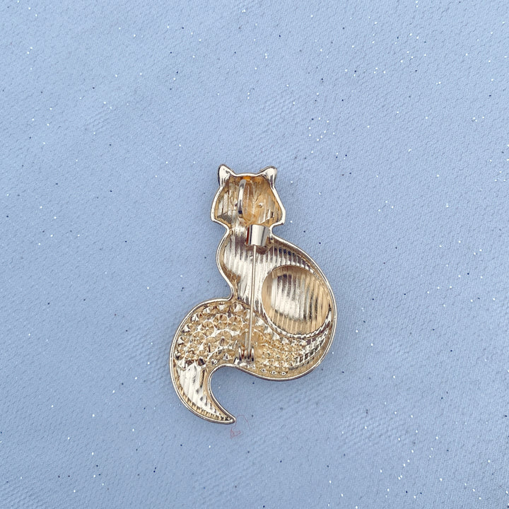 Brown and white fox brooch with blue eyes and an orange crystal tail.