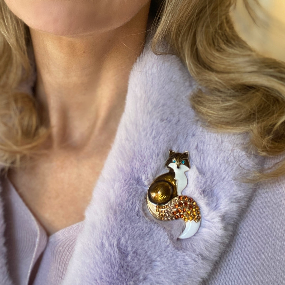 Brown and white fox brooch with blue eyes and an orange crystal tail.