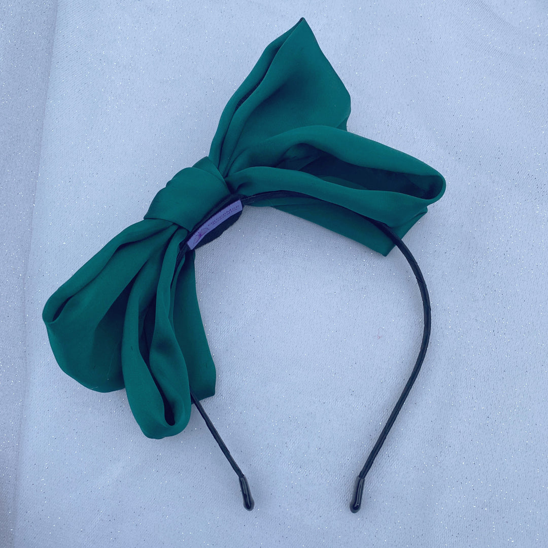 Green oversized bow fascinator on a thin black headband.