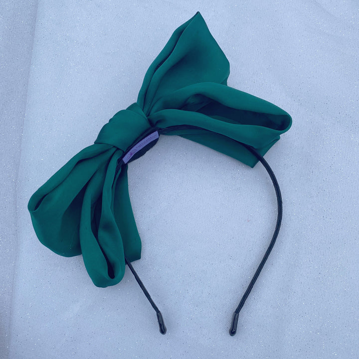 Green oversized bow fascinator on a thin black headband.