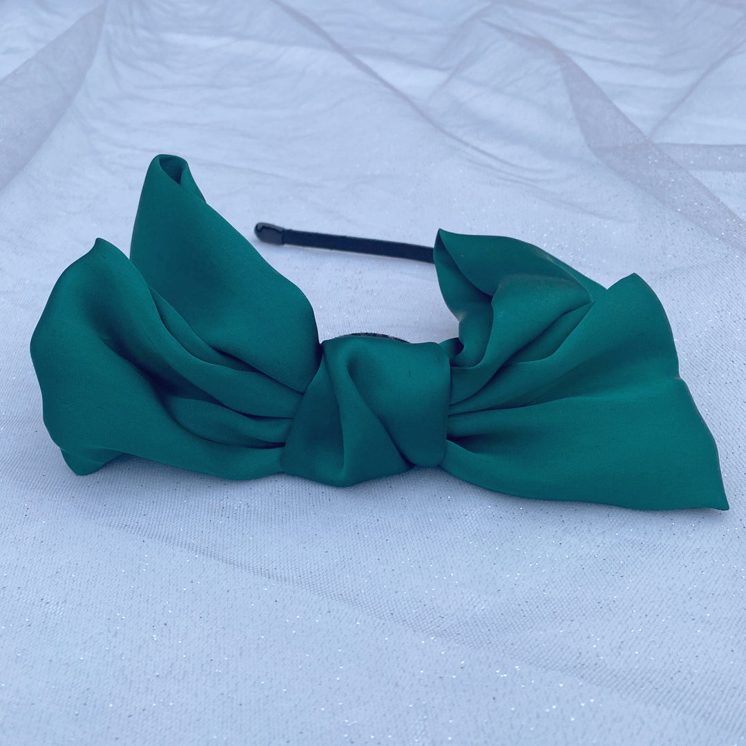 Green oversized bow fascinator on a thin black headband.