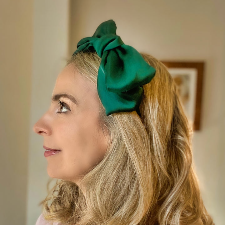 Green oversized bow fascinator on a thin black headband.
