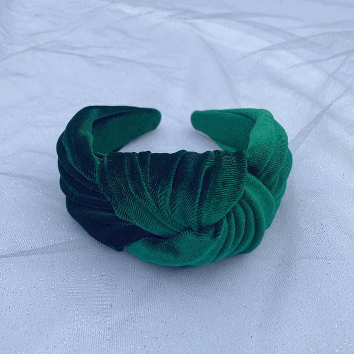 Green velvet knot headband with a wide, padded design on a white fabric background.