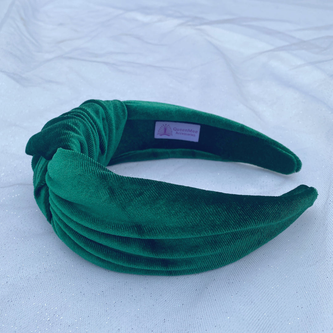 Green velvet knot headband with a wide, padded design on a white fabric background.