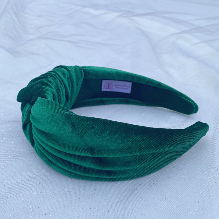 Green velvet knot headband with a wide, padded design on a white fabric background.