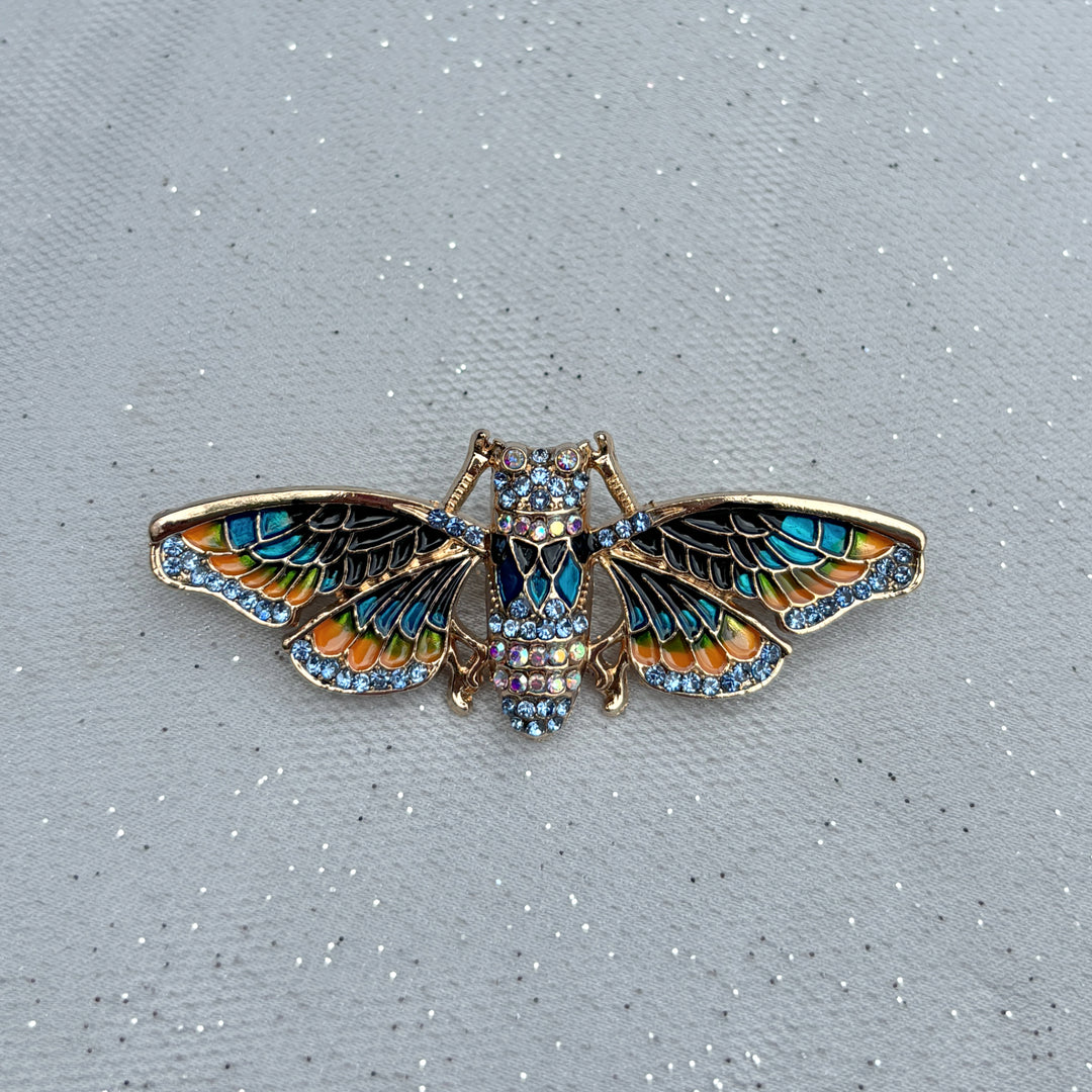 Moth brooch, gold tone metal, enamel wings in blue and orange with black detailing, body encrusted with clear crystals, nature inspired jewellery design, vintage style accessory, unique statement brooch, elegant gift for her
