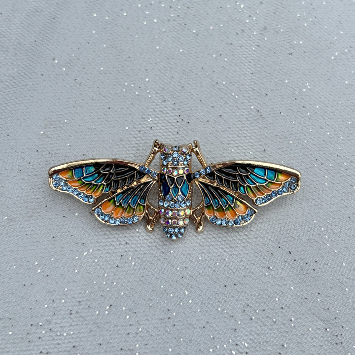 Moth brooch, gold tone metal, enamel wings in blue and orange with black detailing, body encrusted with clear crystals, nature inspired jewellery design, vintage style accessory, unique statement brooch, elegant gift for her
