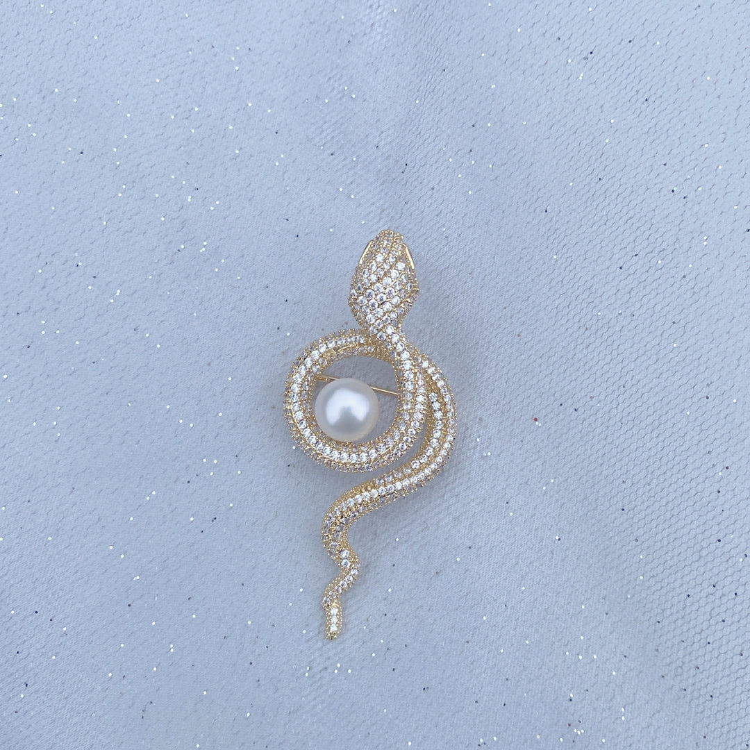 Gold snake brooch with sparkling crystals wrapped around a white pearl.