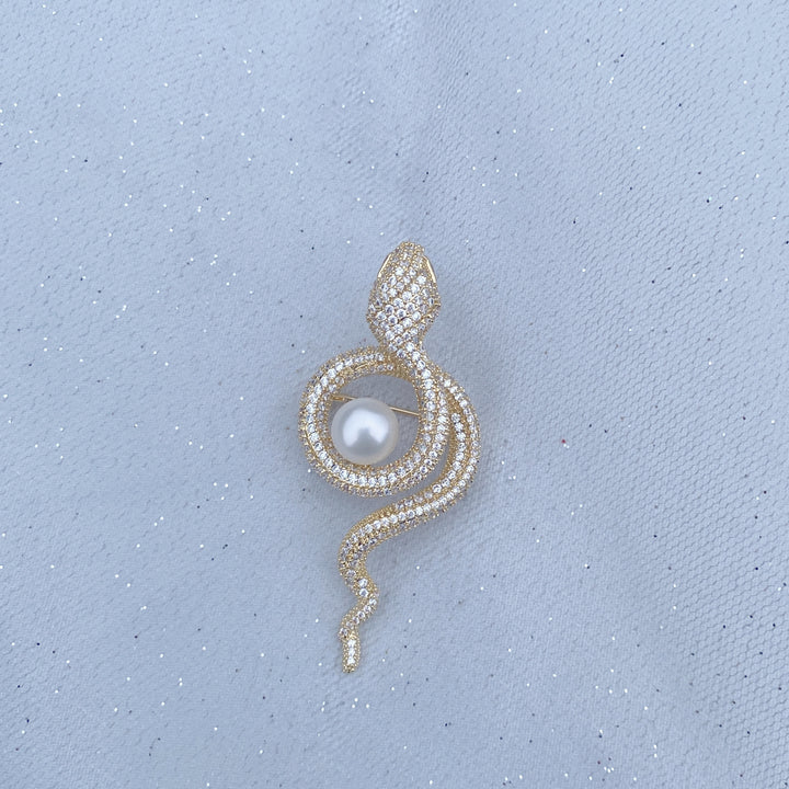 Gold snake brooch with sparkling crystals wrapped around a white pearl.